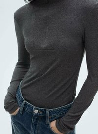 Haut ajusté à manches longues de couleur gris foncé avec un col haut et un détail de patch rectangulaire à l'avant, porté rentré dans un jean bleu taille haute.