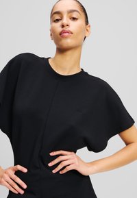 T-shirt nera oversize con maniche corte, scollo rotondo e dettagli cuciti. Presenta un ricamo del logo discreto sul petto.