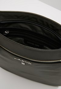 Sort nylon håndtaske med sølvfarvet hardware, der har flere lynlåslommer og en glat tekstur. Indvendig foring er mørk.