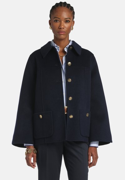 Kabát z námorníckej modrej vlnenej zmesi so štruktúrovaným dizajnom, veľkými gombíkmi v zlatom tóne a dvoma prednými vreckami. Má golierový výstrih a rozšírené rukávy.