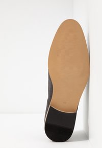 Chaussure en daim noir avec un bout arrondi, une texture lisse et une semelle en caoutchouc beige clair affichant un motif côtelé. Taille 42 indiquée sur la semelle.