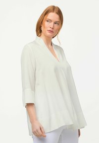 Weiße, leichte Bluse mit V-Ausschnitt, 3/4-Ärmeln und ausgestelltem Saum. Glatte Textur mit minimalistischem Design. Keine sichtbaren Muster oder Akzente.