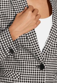 Zwart-witte ruit blazer met notch lapels, enkele knoopsluiting en een gestructureerde stof; heeft een getailleerde pasvorm en zichtbare zak.