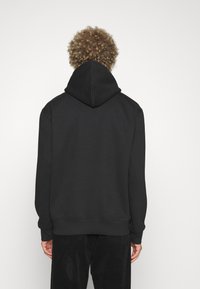 Svart hettegenser med snøring, ribbestrikkede mansjetter og kant, laget av mykt stoff. Bakvisning viser et ensfarget design uten grafikk.