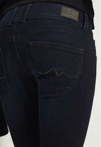 Mörkblå denimjeans med en figurnära design. Bakfickor med dekorativa mönster och nitar. Läderetikett på midjebandet.