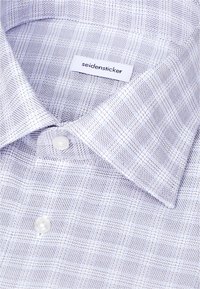 Chemise blanche à motifs avec col pointu et deux boutons blancs, étiquetée « seidensticker » à l'intérieur du col.