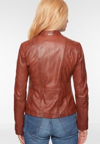 Braune Lederjacke mit tailliertem Schnitt, featuring Nahtdetails und steigendem Kragen. Die Textur ist glatt mit einem leichten Glanz.