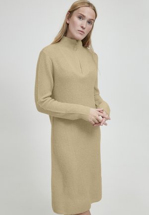 Abito lavorato a maglia beige con colletto alto, maniche lunghe e zip a un quarto. Presenta un design a costine testurizzato e una silhouette fino al ginocchio.