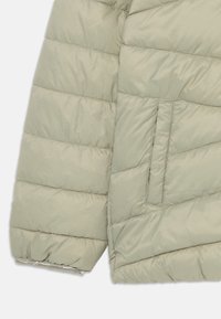 Veste rembourrée gris clair avec des coutures diagonales, dotée d'une poche latérale extérieure et d'ourlets de manches élastiques pour un ajustement confortable.