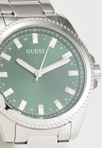 Orologio in acciaio inox con quadrante verde metallico, indici delle ore argentati e lancette luminescenti. Presenta una lunetta testurizzata e un bracciale a maglie.