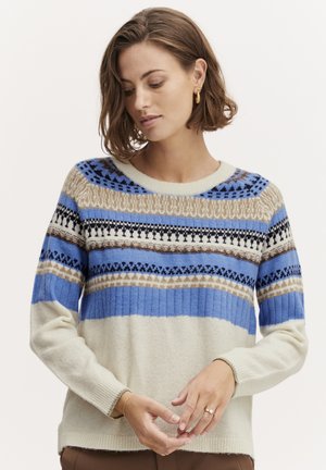 Sweater in cream, blue, and brown with a patterned knit design. Features a ribbed texture and round neckline. Long sleeves, relaxed fit.