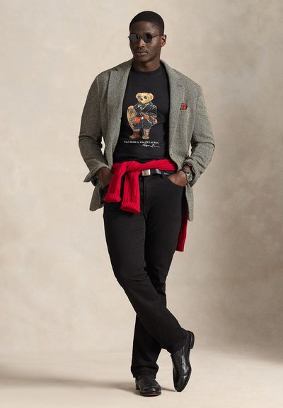 Grå sildebensmønstret blazer over svart grafisk t-skjorte med panda. Rød genser knyttet rundt livet, svarte jeans og svarte sko.