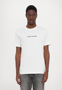 Fehér pamut póló, kerek nyakkivágással és rövid ujjakkal, az elülső részen fekete betűkkel "ARMANI EXCHANGE" felirattal.