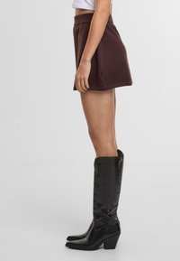 Brun stickad minikjol med utställd form, kombinerad med knähöga svarta läderstövlar med en kraftig klack.