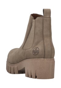 Botín de ante marrón con paneles laterales elásticos, suela de goma texturizada, tacón grueso y un logo circular en el lado.