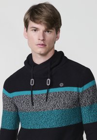 Suéter de punto en negro con rayas horizontales en verde azulado y gris. Presenta un cuello alto y cierre con cordones con acentos grises. Tejido texturizado.