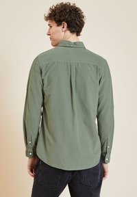 Hemd met lange mouwen in gedempt olijfgroen stof. Voorzien van een button-down kraag, een knopenlijst en een ronde zoom. Glad van textuur.