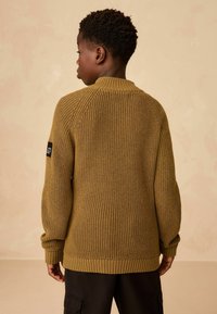 Strickpullover in Olivgrün mit geripptem Material, Rundhalsausschnitt, überschnittenen Schultern und einem Patch am linken Ärmel.
