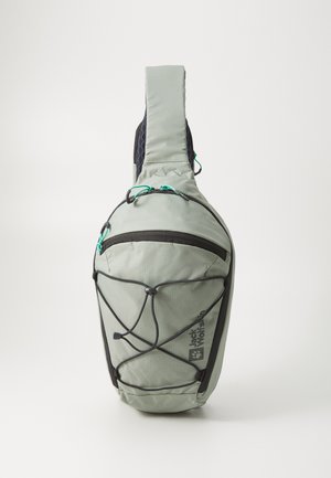 Crossbody backpack in light green fabric. Features a zippered main compartment, bungee cord detailing, and padded shoulder strap.