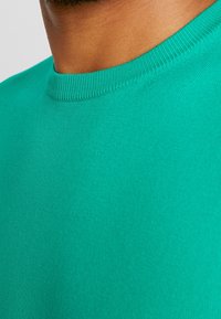 Turkusowa koszulka z okrągłym dekoltem wykonana z miękkiego materiału. Posiada gładką, równą strukturę z prążkowanym dekoltem.