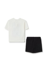 Camiseta blanca de algodón de manga corta con un detalle de botón en la parte posterior, combinada con pantalones cortos negros con cintura elástica.