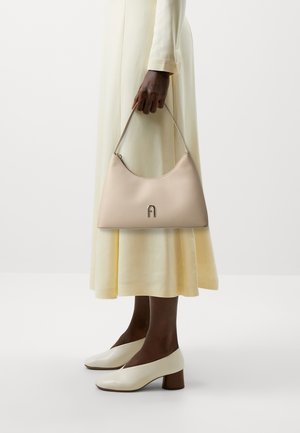 Béžová kožená kabelka s oblým designem, s stříbrným logem a jedním ramenním popruhem. Texturovaný povrch s hladkým vzhledem.