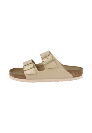 Beige Birkenstock-sandaal met twee verstelbare bandjes, metalen gespen, kurken binnenzool en witte gestructureerde zool, zijaanzicht.