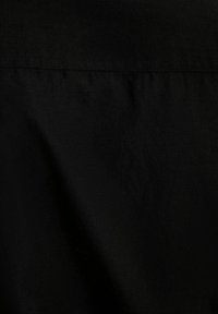 Tessuto nero con una texture liscia, caratterizzato da pieghe sottili e una finitura opaca. Il materiale sembra leggero e si drappeggia morbidamente.