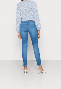 Světle modré skinny džíny s hladkou denimovou texturou a středně vysokým pasem, spárované s bílou blůzou s modrým puntíkovým vzorem.