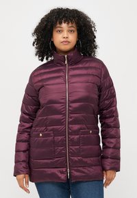 Burgundy puffer jacket with a high collar, zip closure, two front pockets, and subtle gold hardware accents; quilted texture throughout.