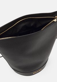 Borsa a secchiello nera in pelle con finitura testurizzata, zip dorata e dettaglio del logo metallico alla base. L'interno presenta una fodera nera uniforme.