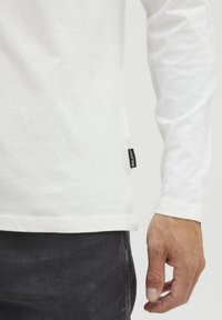 Langærmet hvid t-shirt lavet af blød bomuld, med en lige kant, sideetiket og tætsiddende ærmer, kombineret med mørke jeans.