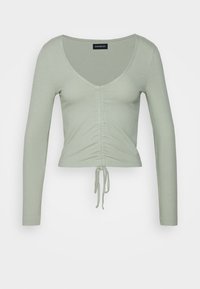 Langärmliges grünes Rippoberteil mit tiefem V-Ausschnitt, gerafftem Detail an der Vorderseite und verstellbarem Kordelzug am Saum.