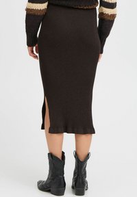 Ribbeliger brauner Strickrock mit einem seitlichen Schlitz, der eine taillierte Silhouette bietet. Kombiniert mit schwarzen Cowboy-Stiefeln für einen kontrastierenden Look.