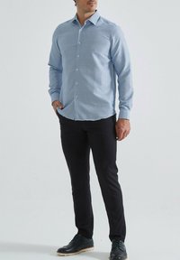 Chemise à manches longues bleu clair à motifs, devant boutonné, avec un col, assortie à un pantalon noir et des chaussures noires.