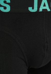 Ropa interior negra con una cintura ancha y texturizada en color verde azulado que muestra el nombre "JACK", con costuras planas para mayor comodidad y un acabado suave.