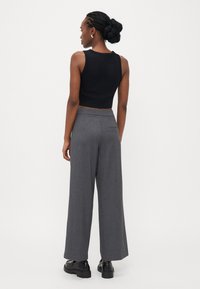 Sort cropped tank top parret med grå brede bukser. Bukserne har en subtil tekstur og en baglomme, fuldendt med sorte sko.
