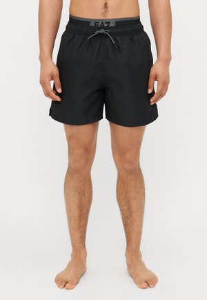 Black swim shorts with an elastic waistband, drawstring detail, and smooth texture. Features logo on the waistband and side slits.