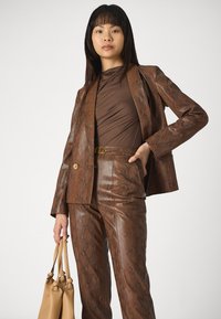 Bruin met slangenhuidpatroon blazer en broek set met een gladde textuur, gecombineerd met een aansluitend bruine top en een beige handtas.