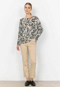 Haut à manches longues avec un motif floral dans des nuances de vert, beige et noir. Assorti à un pantalon droit beige et des mocassins noirs.