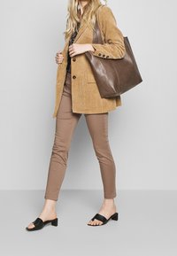 Een tan corduroy blazer, een patroon top, bruin aangesloten broek en zwarte slide sandalen. Een bruine leren tote bag met een zachte textuur en een gestructureerde vorm.
