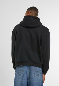 Sort hættetrøje med afslappet pasform, der har ribbet kant og manchetter, parret med løse blå denimshorts. Mat tekstur.