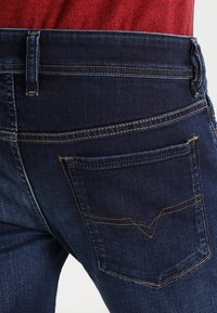 Mörkblå denimjeans med en åtsittande form, med en bakfick som har en distinkt V-formad sömdetalj.