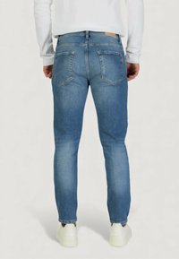Jeans de mezclilla azul con corte recto, que cuentan con dos bolsillos traseros y combinan con zapatillas blancas. Textura suave con un desvanecimiento mínimo.