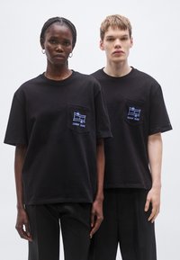 Čierne bavlnené tričká s krátkym rukávom a náprsným vreckom, so modrým vyšívaným logom. Jednoduchý, pohodlný strih.