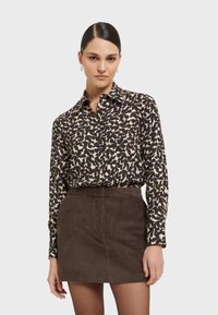 Zwart en beige gestreepte lange-mouwen shirt met een knoopkraag, gecombineerd met een bruine corduroy mini-jurk met verticale strepen.