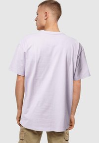 Camiseta oversized en color lila, hecha de algodón, con cuello redondo y mangas cortas, de textura suave y diseño minimalista.