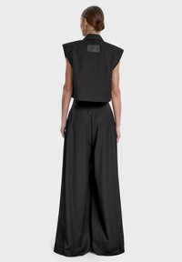 Czarny krótki top z szerokimi ramiączkami, w połączeniu z luźnymi czarnymi spodniami o wysokim stanie. Obie rzeczy wykonane są z fakturowanej tkaniny i mają minimalne akcenty.