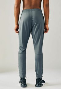 Herre sportbukser i grå, med en tætsiddende pasform, elastisk talje og sidelommer. Stof er glat med let glans.