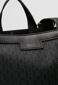 Sac à main en cuir noir texturé avec des poignées courtes, comportant un petit logo Hugo Boss embossé sur le panneau avant près du bord supérieur.